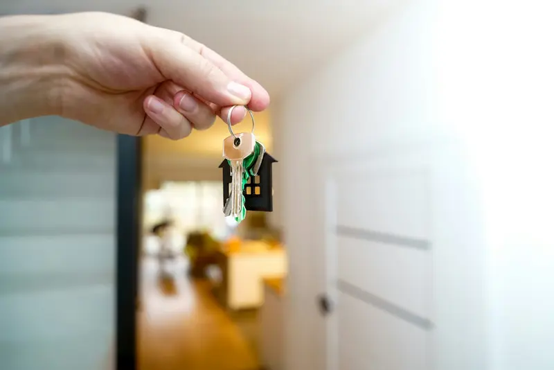 A hand holding a set of house keys at an open front door