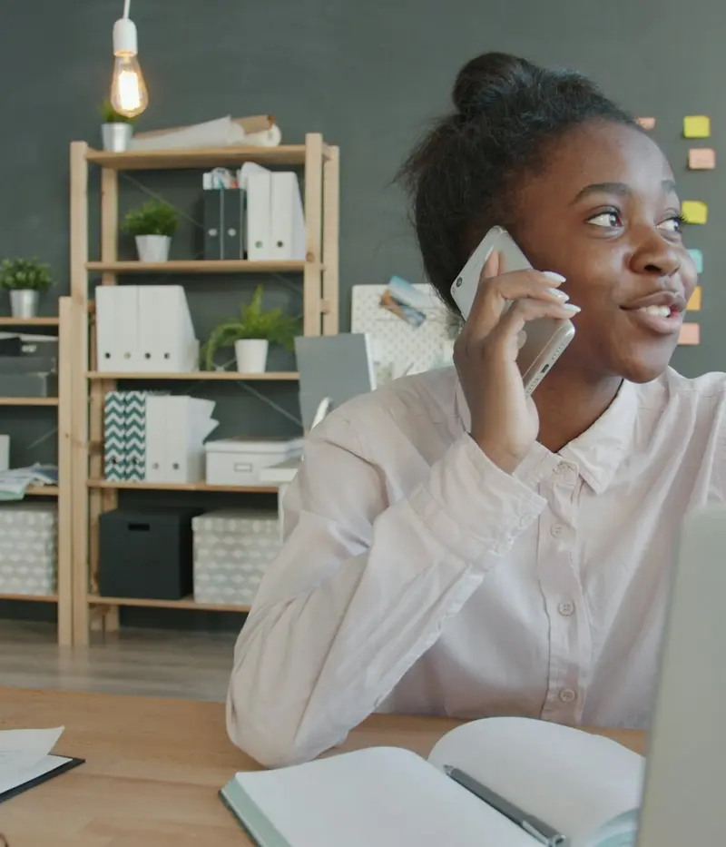 A smiling woman on a phone call at her desk