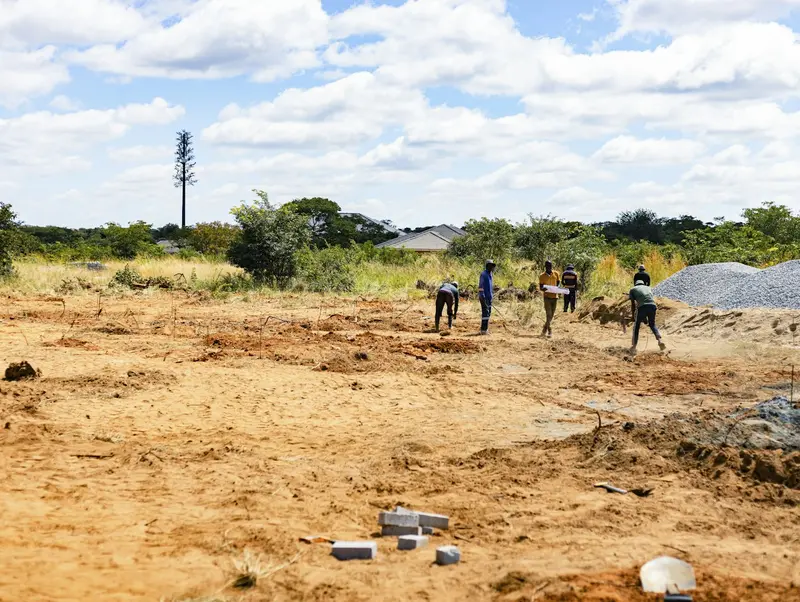 People surveying an open plot of cleared land under a blue sky